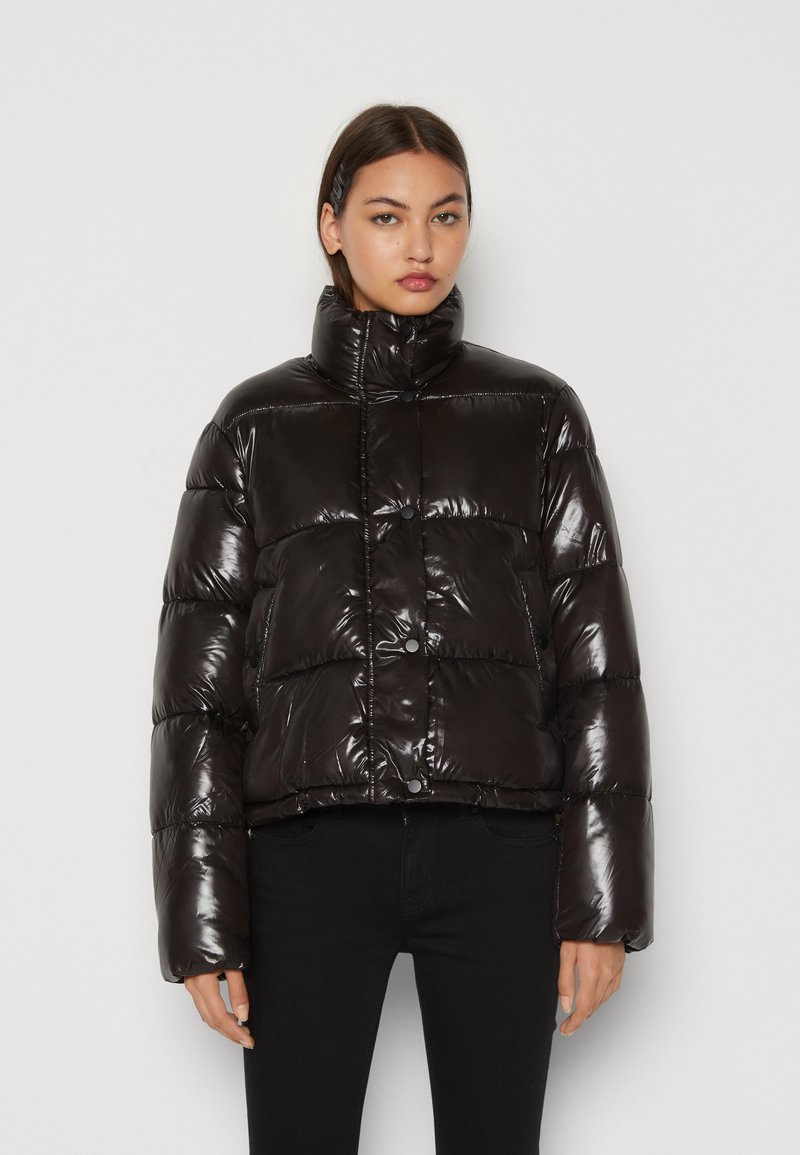 Chaqueta de plumas negra con acabado brillante, cuello alto, botones a presión y diseño corto. Presenta secciones acolchadas y mangas amplias.