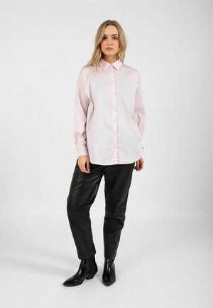 Svetloružová košeľa na zapínanie s golierom, v kombinácii s čiernymi koženými nohavicami a špicatými čiernymi topánkami. Hladká textúra a pohodlný strih.