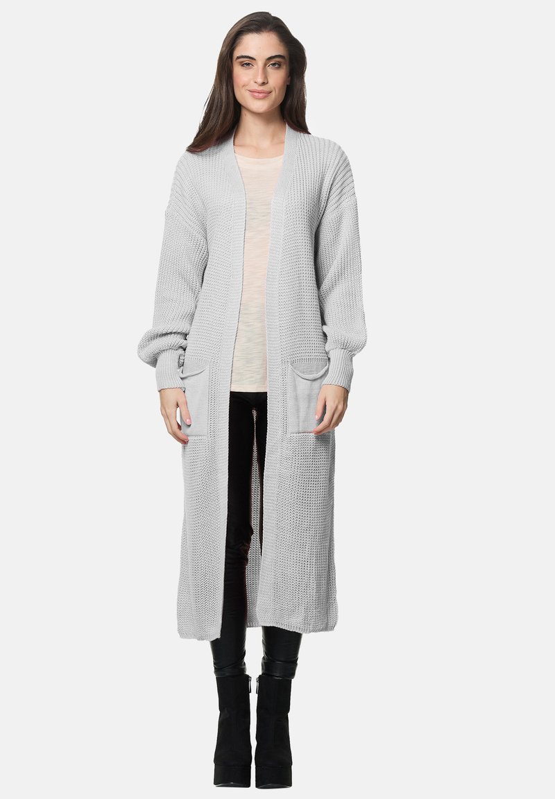 Lång, ljusgrå stickad cardigan med öppen framsida, ribbade manschetter och två framfickor. Texturerat mönster, i kombination med en krämfärgad topp och svarta byxor.