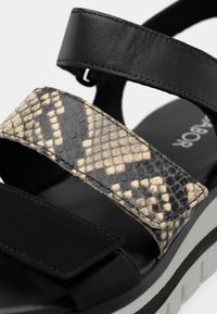 Μαύρα σανδάλια με λωρίδες σε σχέδιο φίδι, με υφή. Παχύ πέλμα με λευκές και γκρι λεπτομέρειες. Κλείσιμο με βέλκρο στις λωρίδες.