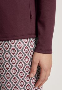 Langarmige bordeauxrode top van gladde stof, gecombineerd met gepatternde leggings met florale en druppelmotieven in bordeaux, roze en blauw.