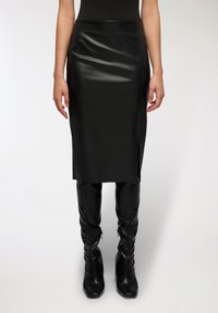 Gonna midi in pelle nera con una texture liscia e elegante e spacchi laterali, abbinata a stivali neri attillati fino al ginocchio.