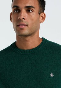 Grüner Strickpullover mit einem gerippten Kragen und Struktur. Verfügt über ein kleines Pinguin-Logo auf der linken Brust.