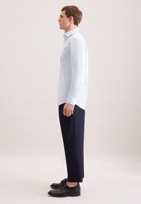 Hellblau-weiß gestreiftes Hemd mit Knöpfen, kombiniert mit marineblauen Hosen und schwarzen Schuhen, seitlich dargestellt.