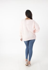 Lichtroze oversized trui met lange mouwen en geribbeld uiteinde, gecombineerd met aansluitende blauwe jeans en doorzichtige blokhak schoenen.