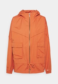 Oranger, lättviktsjacka med huva, dragkedja framtill, två framfickor, dragsko i nederkant och elastiska ärmslut. Strukturerad tyg med synlig sömnad.