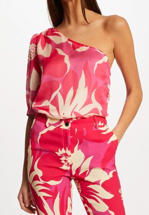 En skulder pink bluse med blomsterprint og silkeagtig tekstur, kombineret med matchende bukser med store blomsterprint i lignende farver.