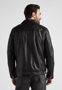 Svart läderjacka med klassisk krage, tryckknappsmuddar och sydda detaljer. Slät textur, figursydd passform och minimalistisk design.