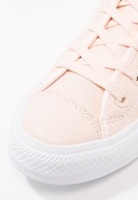 Helle rosa Turnschuhe mit strukturiertem Synthetik-Obermaterial, runder weißer Gummisohle und flachen Schnürsenkeln. Zu den Merkmalen gehören durchbrochene Details und Metallösen.