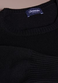 Musta neulepusero, jossa on resorilla viimeistelty kaula-aukko ja hihansuut. Labeli kertoo "Drumohr, Established 1770." Sileä pinta ja klassinen muotoilu.