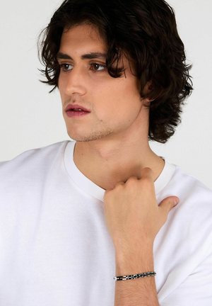 Braccialetto nero e argento su un polso, caratterizzato da un design geometrico, una texture metallica liscia e una finitura lucida. Il polso è scoperto.