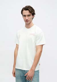 Λευκό κοντομάνικο μπλουζάκι με στρογγυλή λαιμόκοψη, με ροζ λογότυπο "DIESEL" στο αριστερό στήθος. Κατασκευασμένο από ελαφρύ βαμβακερό ύφασμα.