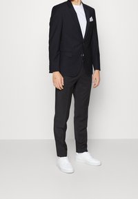 Blazer blu navy con rever a picco, t-shirt bianca, pantaloni scuri e sneakers bianche. Presenta un fazzoletto da taschino e un design slim fit.