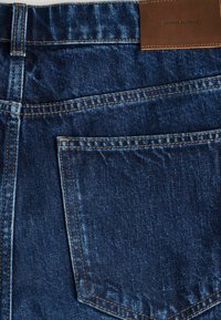 Jeans de mezclilla azul con un bolsillo trasero detallar con costuras en contraste. Cuenta con una etiqueta de cuero marrón en la cinturilla.