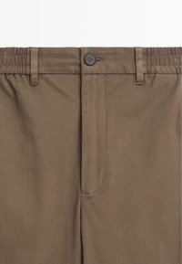Bruine broek met een gladde textuur, knoopsluiting en een elastische tailleband. Inclusief riemlussen en zijzakken.