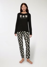 Maglietta da pigiama a maniche lunghe nera con grafiche di panda e testo; pantaloni neri a fantasia con forme di nuvole bianche. Tessuto di cotone morbido, vestibilità comoda.