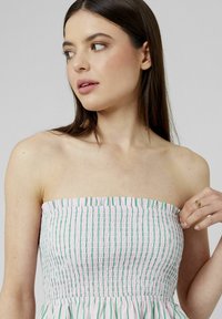 Robe sans bretelles avec un design rayé rose et blanc, accentuée de vert, fabriquée en tissu froncé. Texture lisse et silhouette ajustée.