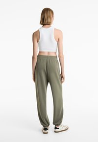 Hvid ribbet cropped top og olivengrønne tapered sweatpants med elastisk talje og manchetter, parret med beige og sorte sneakers.