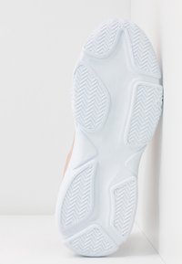 Semelle blanche de basket avec motifs antidérapants texturés sur plusieurs sections, inclinée contre une surface blanche angulaire.