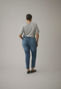 Grå randig t-shirt, blå skinny jeans och svarta ballerinaskor. Mjuk tyg, figurnära design, med bakfickor och en synlig etikett i midjan.