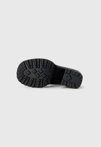 Semelle de chaussure noire avec des rainures profondes et des motifs en forme de croix, conçue pour offrir une adhérence sur des surfaces lisses.