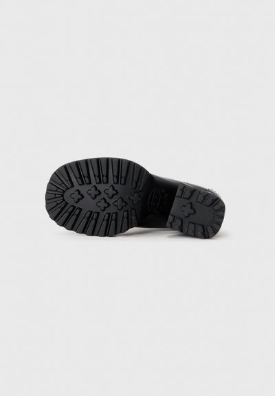 Semelle de chaussure noire avec des rainures profondes et des motifs en forme de croix, conçue pour offrir une adhérence sur des surfaces lisses.