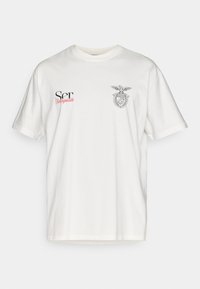 Biała koszulka z krótkim rękawem wykonana z bawełny, z stylizowanym emblematem orła oraz logo w czerni i czerwieni z przodu. Klasyczny krój z okrągłym dekoltem.