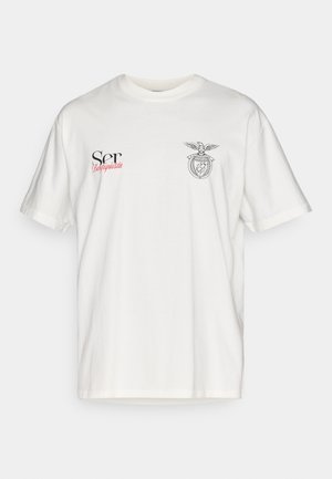 T-shirt bianco a maniche corte in cotone con un emblema stilizzato di aquila e loghi neri e rossi sul davanti. Design classico con scollo rotondo.