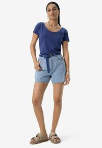 Haut bleu marine à manches courtes, short taille haute à rayures verticales bleu clair avec ceinture, et sandales tan à glissière avec des brides tressées.