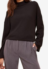 Musta, pitkähihainen neulepaita, jossa on korkea kaulus ja rento fit; yhdistettynä vaaleanharmaisiin, laskostettuihin housuihin. Sileä pinta, rento tyyli.