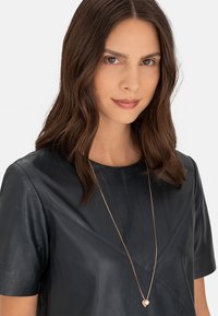 Zwart leren top met korte mouwen, een gladde textuur en diagonale naaddetails, gecombineerd met een roségouden ketting met een hartje.