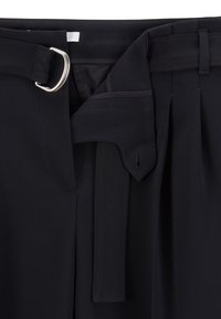 Lähikuva mustista pökistä, joissa on D-rengaspuristuksen vyölenkki ja osittain auki oleva vyötärö, joka paljastaa ommellut yksityiskohdat ja vyöreiät.