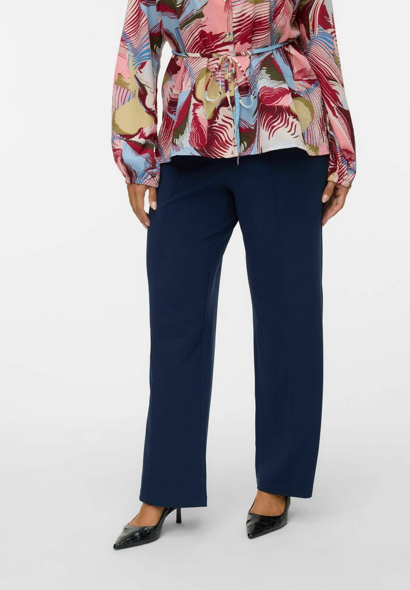 Un pantalon large bleu marine associé à un blouse vibrante et à motifs présentant des nuances de rouge, rose et bleu, avec un détail de taille cintrée.