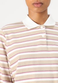 Striped polo shirt in beige with white, pink, and black stripes; features a white collar and two-button placket; made of soft cotton.