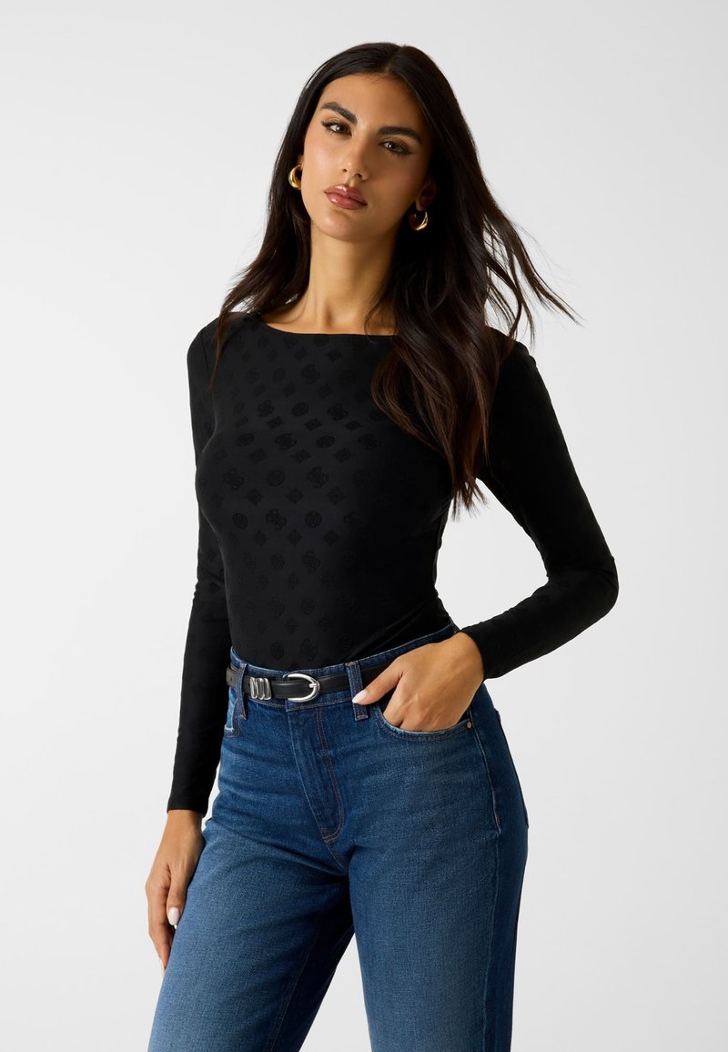 Czarna bluzka na długi rękaw z teksturowanym wzorem, zestawiona z wysokim stanem niebieskich dżinsów z czarnym paskiem z metalową klamrą.