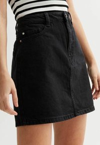 Mustahi denim hameen, jossa on tiukka vyötärö, etutaskut ja suora leikkaus. Varustettu yläpainikkeella ja sivustikkikuvioilla.