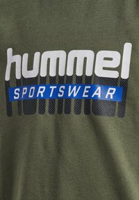 Olivgrön sportt-shirt med fet vit "hummel" text och ett blått "SPORTSWEAR" band, med en texturerad design under.
