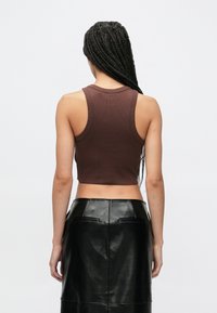 Καφέ ριμπ crop τοπ με στρογγυλή λαιμόκοψη και φαρδιές μασχάλες σε συνδυασμό με μαύρη φούστα μολύβι από συνθετικό δέρμα.