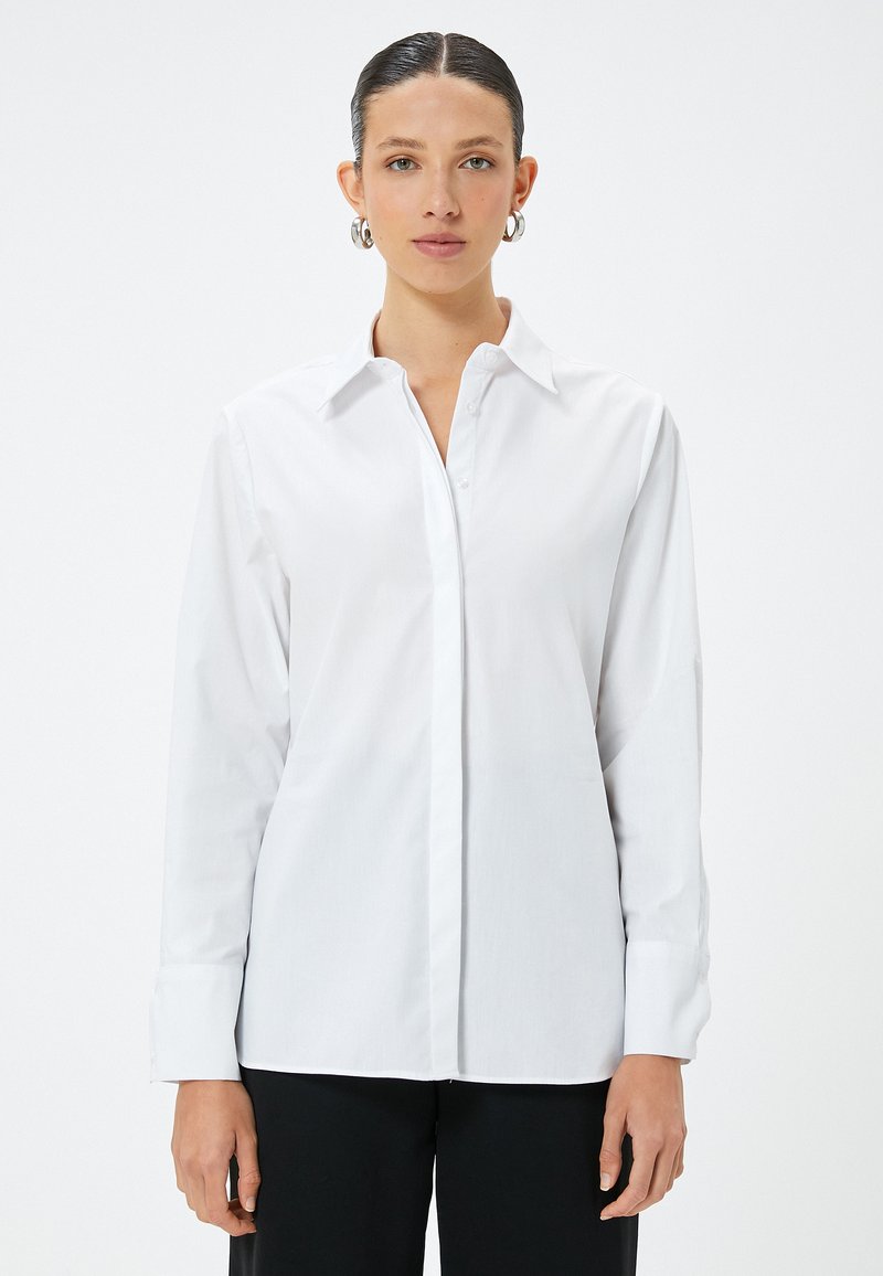 Camicia bianca a maniche lunghe con colletto a punta, chiusura a bottoni sul davanti e tessuto in cotone liscio. Presenta una vestibilità sartoriale e maniche con polsini.