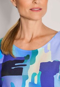 Kurzärmliges Oberteil mit rundem Ausschnitt, gestaltet mit einem geometrischen Muster in Blau-, Lila- und Grüntönen, aus glattem Stoff.