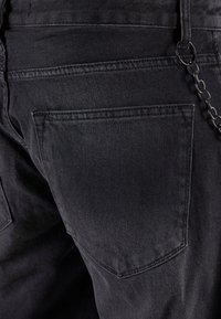 Jeans de mezclilla negra con un acabado texturizado, que cuentan con un bolsillo trasero y un accesorio de cadena unido a la presilla del cinturón.