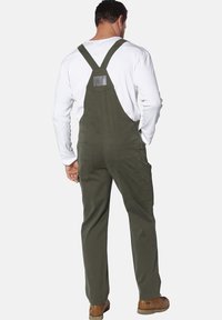 Olivgrüne Latzhose aus strapazierfähigem Stoff; mit verstellbaren Trägern, Seitentaschen und einem rechteckigen Patch nahe des oberen Rückens.