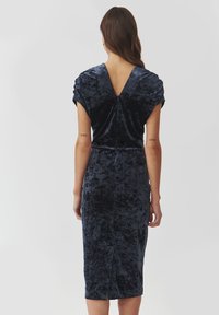 Robe en velours bleu foncé à manches courtes, avec un dos en V et une silhouette ajustée, présentant un léger éclat et une coupe au genou.