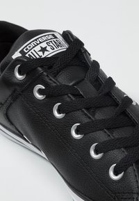 Černé kožené tenisky s kulatou špičkou, černými tkaničkami, kovovými očky a bílou nášivkou. Texturovaný svršek a bílá gumová podrážka.