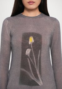 Pulover lung cu maneci lungi, gri și transparent, cu un design floral ce prezintă flori galbene și albe pe un panou mai închis la culoare în centrul său.