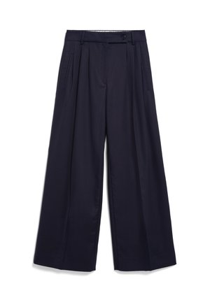 Marineblauwe broek met wijde pijpen, plooien, knoop- en ritssluiting, riemlussen en zijzakken met openingen, plat uitgespreid op een witte achtergrond.