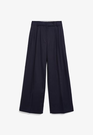 Marineblauwe broek met wijde pijpen, plooien, knoop- en ritssluiting, riemlussen en zijzakken met openingen, plat uitgespreid op een witte achtergrond.