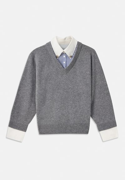 Grauer Strickpullover mit V-Ausschnitt, über einem gestreiften Hemd mit weißem Kragen getragen. Verfügt über kontrastierende weiße Bündchen. Weiche Textur.