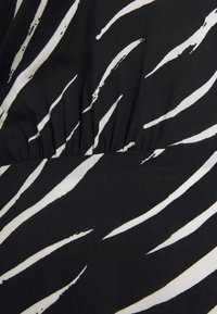 Tissu noir avec des rayures blanches en zigzag, présentant un détail froncé à la taille et une texture globalement lisse.