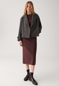 Grijze cropped jack met dubbele knopen, gedragen over een bordeaux ribbeltop en een smalle bordeaux rok; gestyled met zwarte sokken en loafers.